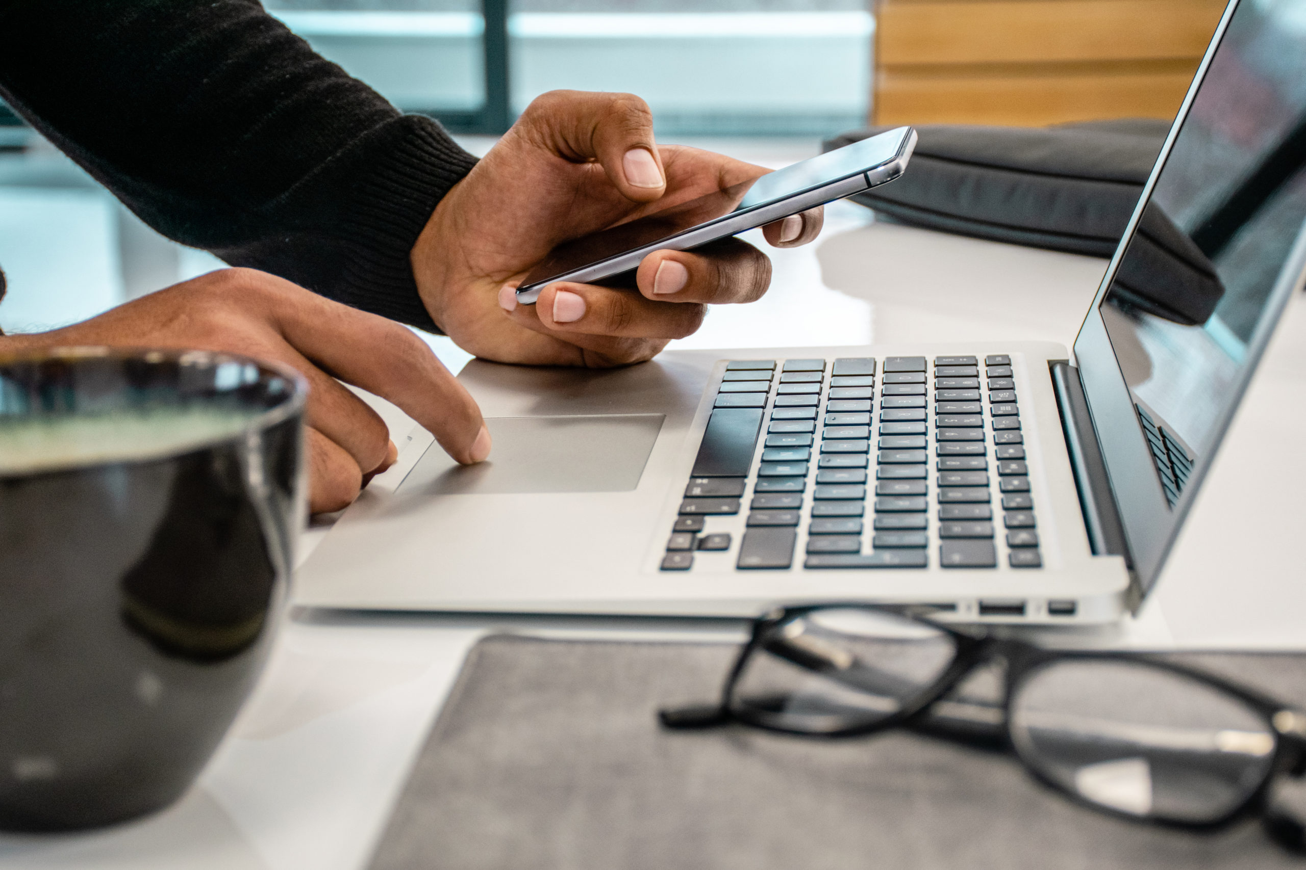 Close up photo of men using phone and laptop